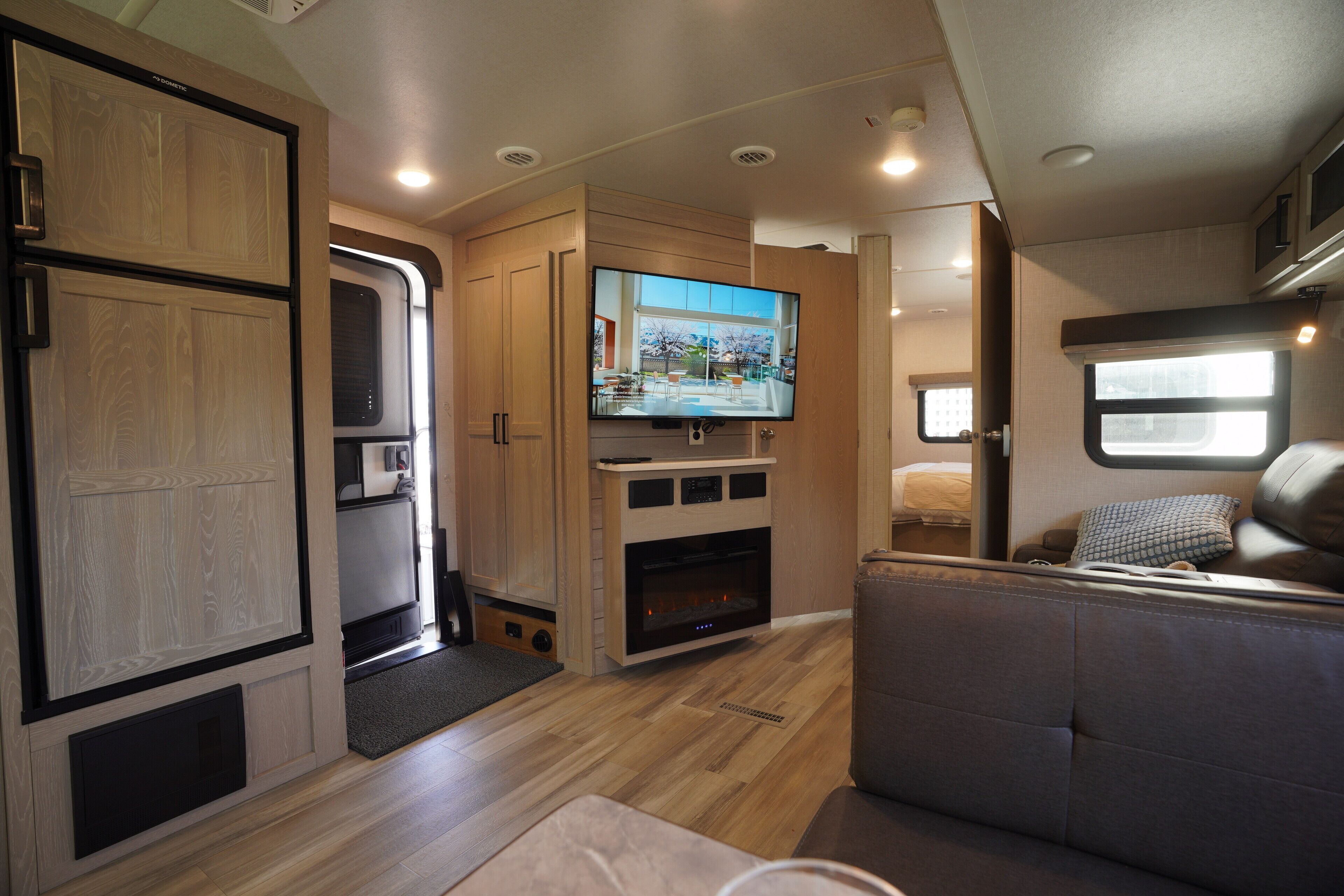 A compact RV interior with a kitchenette, a flat-screen TV, a seating area, and a window providing a view.