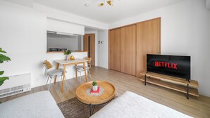Una sala de estar moderna con televisor de pantalla plana, piso de madera, un comedor y un armario grande.