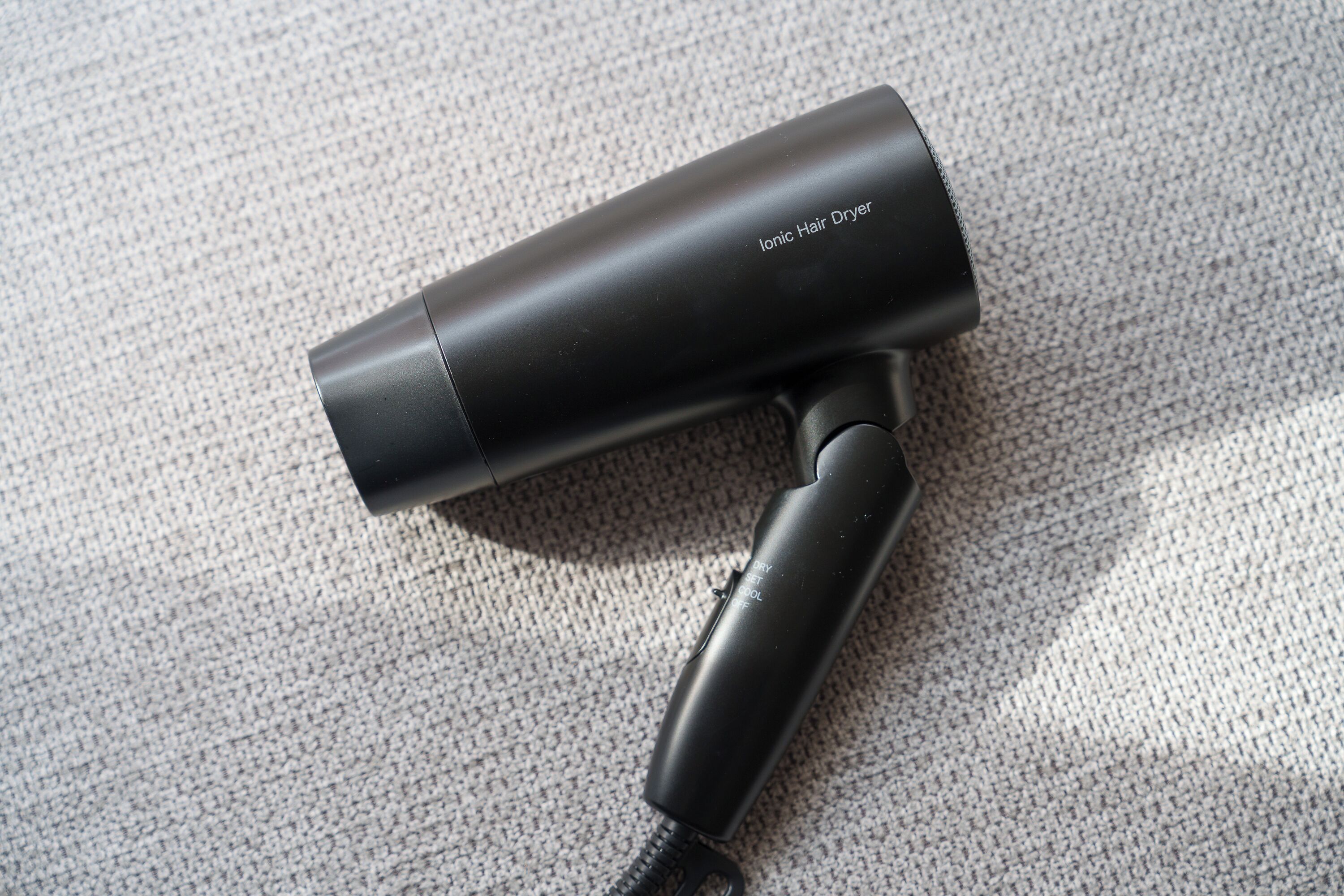 A black ionic hair dryer on a textured carpet.