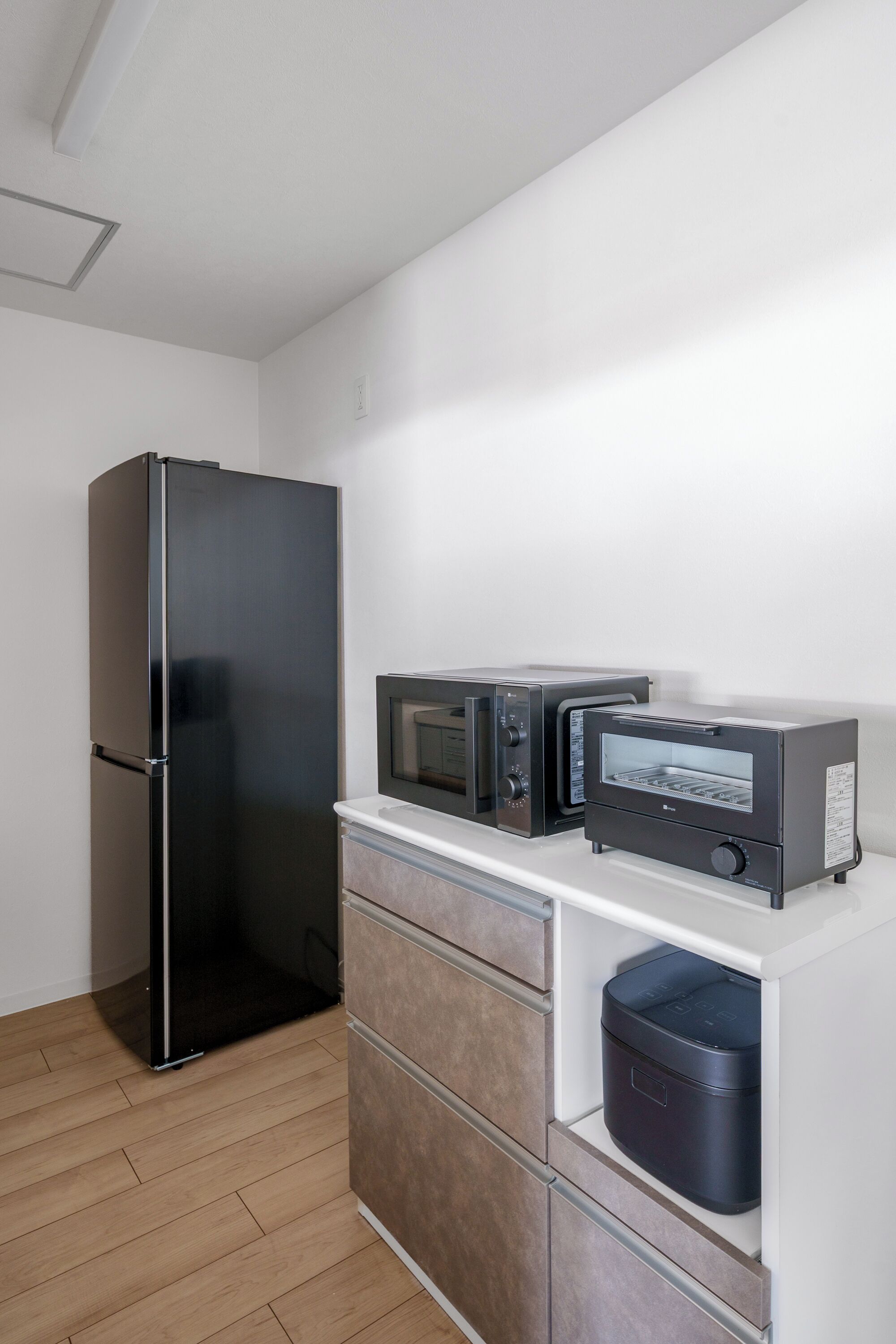 A compact kitchen with a black refrigerator, two black ovens, and a microwave on a white countertop.
