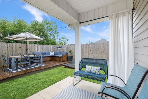 A covered patio with a wooden deck, outdoor furniture, and a view of the backyard.