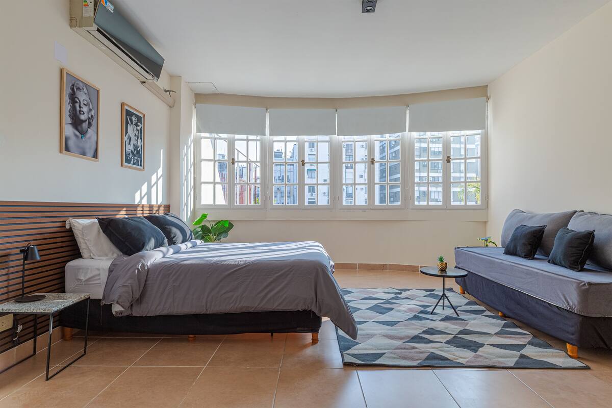 Ein Schlafzimmer mit Bett, einer Couch, einem kleinen Tisch und einem Fenster mit Blick auf Gebäude.