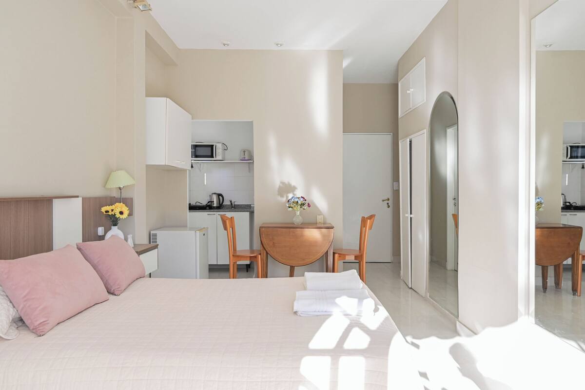 Ein Schlafzimmer mit Bett, Schreibtisch und einer kleinen Küchenzeile im Hintergrund.