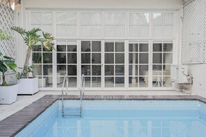 Une piscine avec un escalier en métal, entourée de plantes en pot et d’une clôture blanche.
