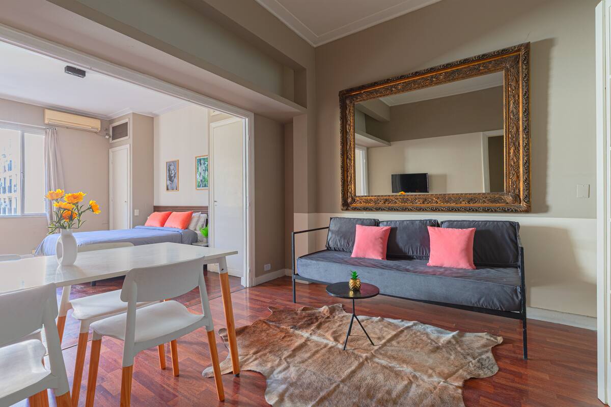 Ein Zimmer mit einer Couch, einem Esstisch mit Stühlen, einem großen Spiegel und einem Fellteppich.
