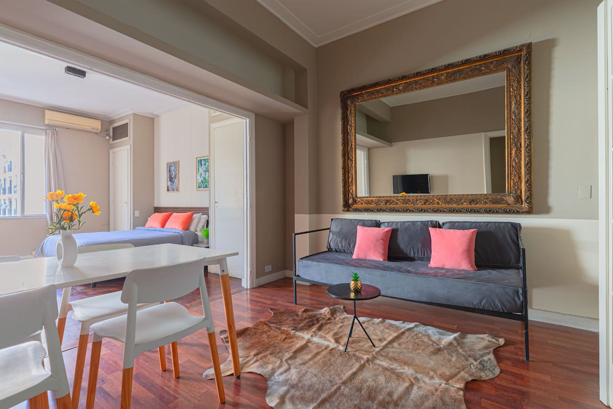 Una habitación con sofá, una mesa de comedor con sillas, un espejo grande y una alfombra de piel.