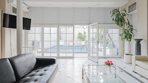 A spacious living area with a black leather sofa, a glass coffee table with pink flowers, and a view of a pool through large glass doors. - Leonardo Da Vinci Aparts by MOT Rentals (Buenos Aires)