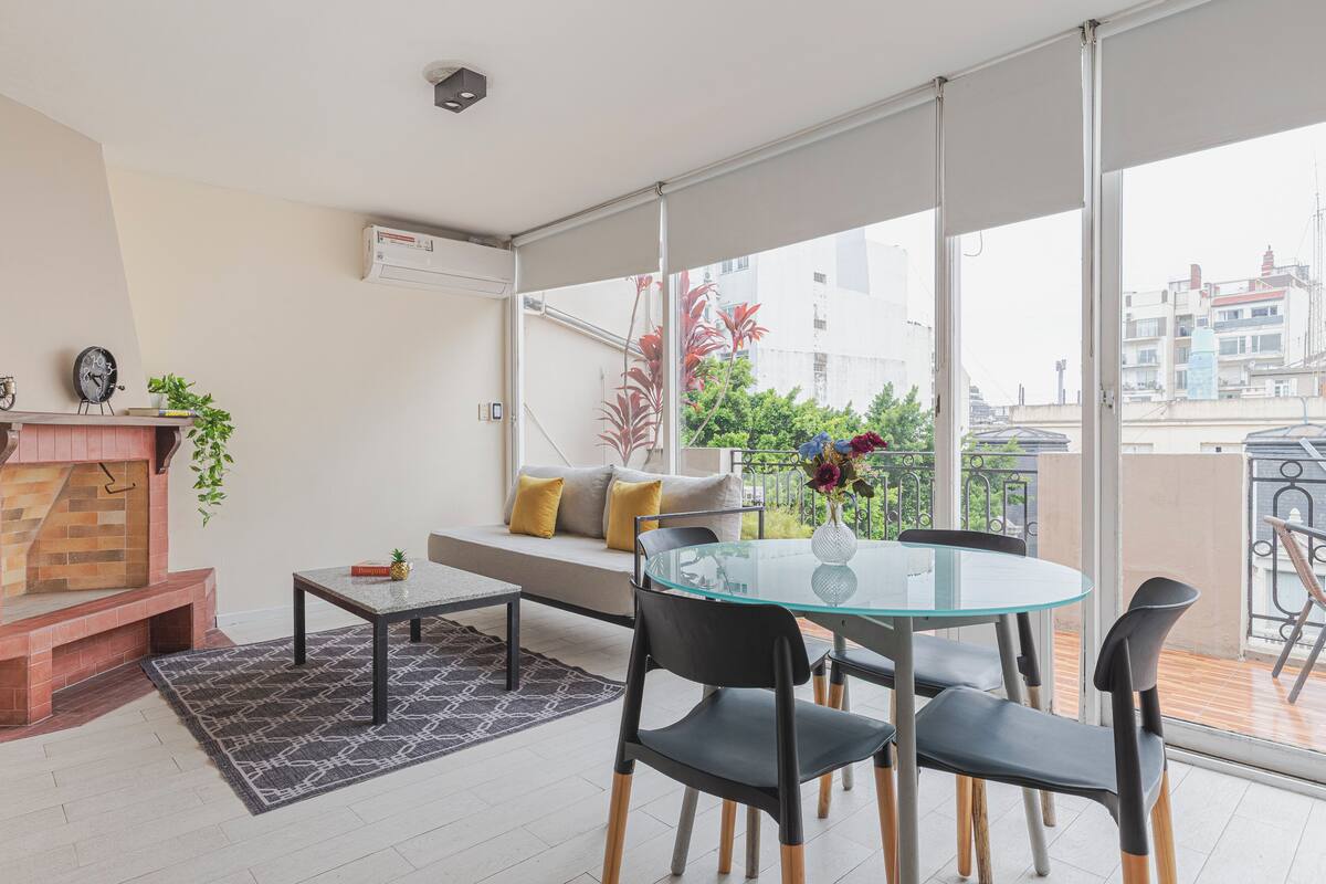 Ein modernes Wohnzimmer mit Glastisch, schwarzen Stühlen, Kamin und Blick auf die Stadt durch große Fenster.