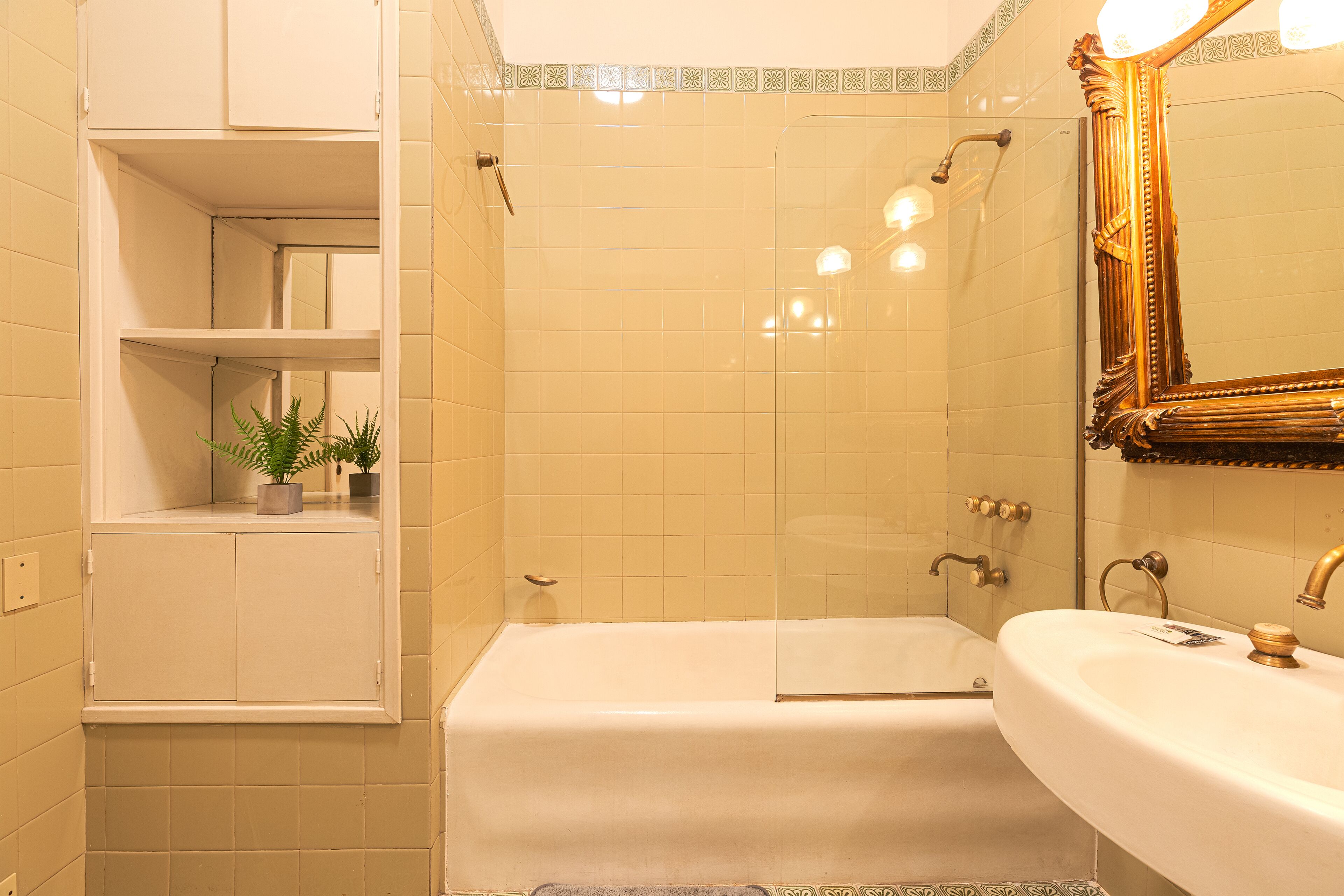 Une salle de bain avec une baignoire, un lavabo, un miroir et une étagère sur laquelle est posée une plante.