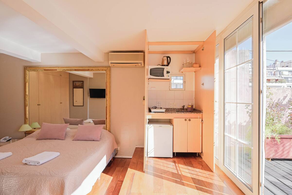 Ein kompaktes Hotelzimmer mit Bett, einer Küchenzeile, einem kleinen Badezimmer und einem Balkon mit Blick.