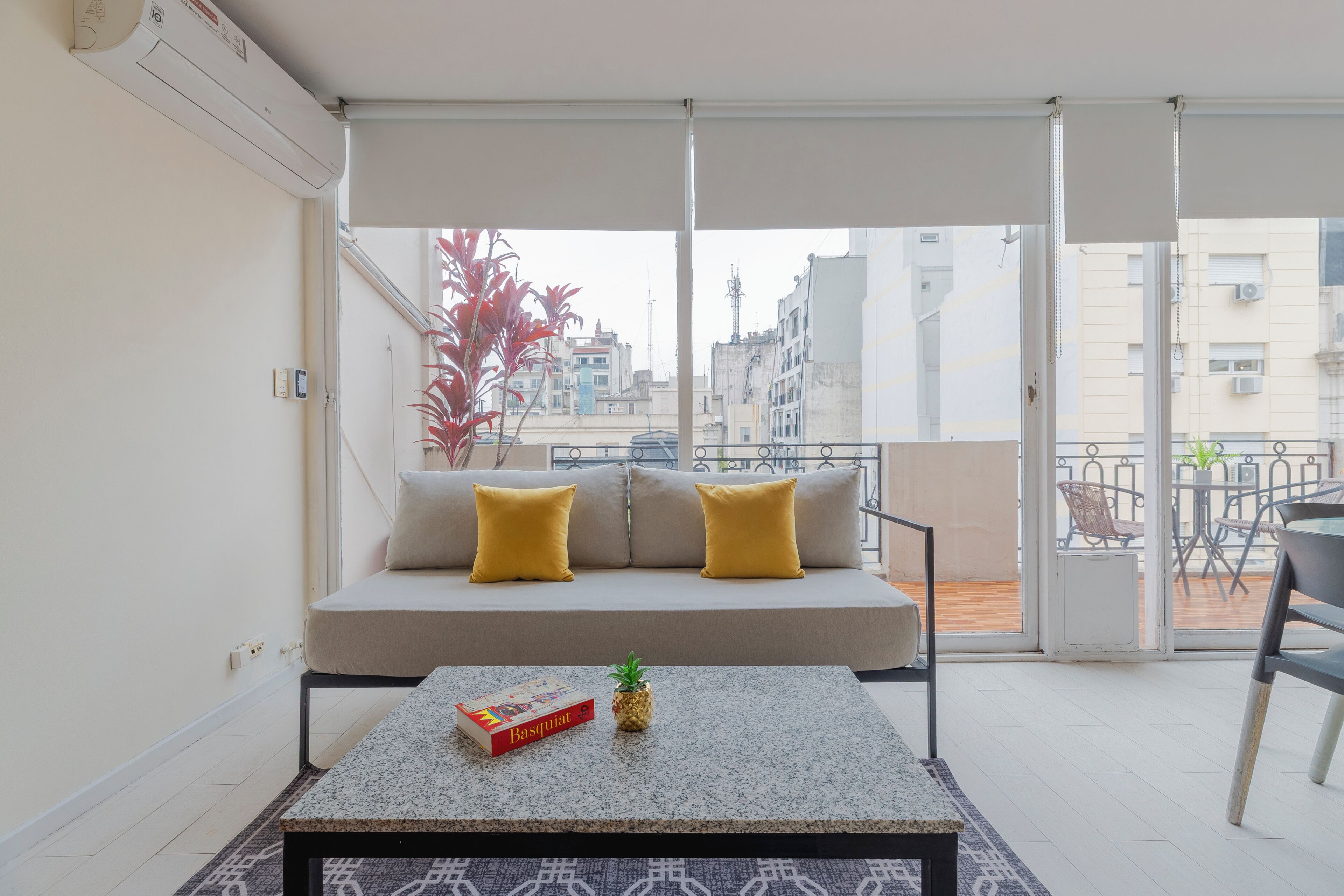 A balcony with a sofa, a table with a book and a plant, and a view of buildings.