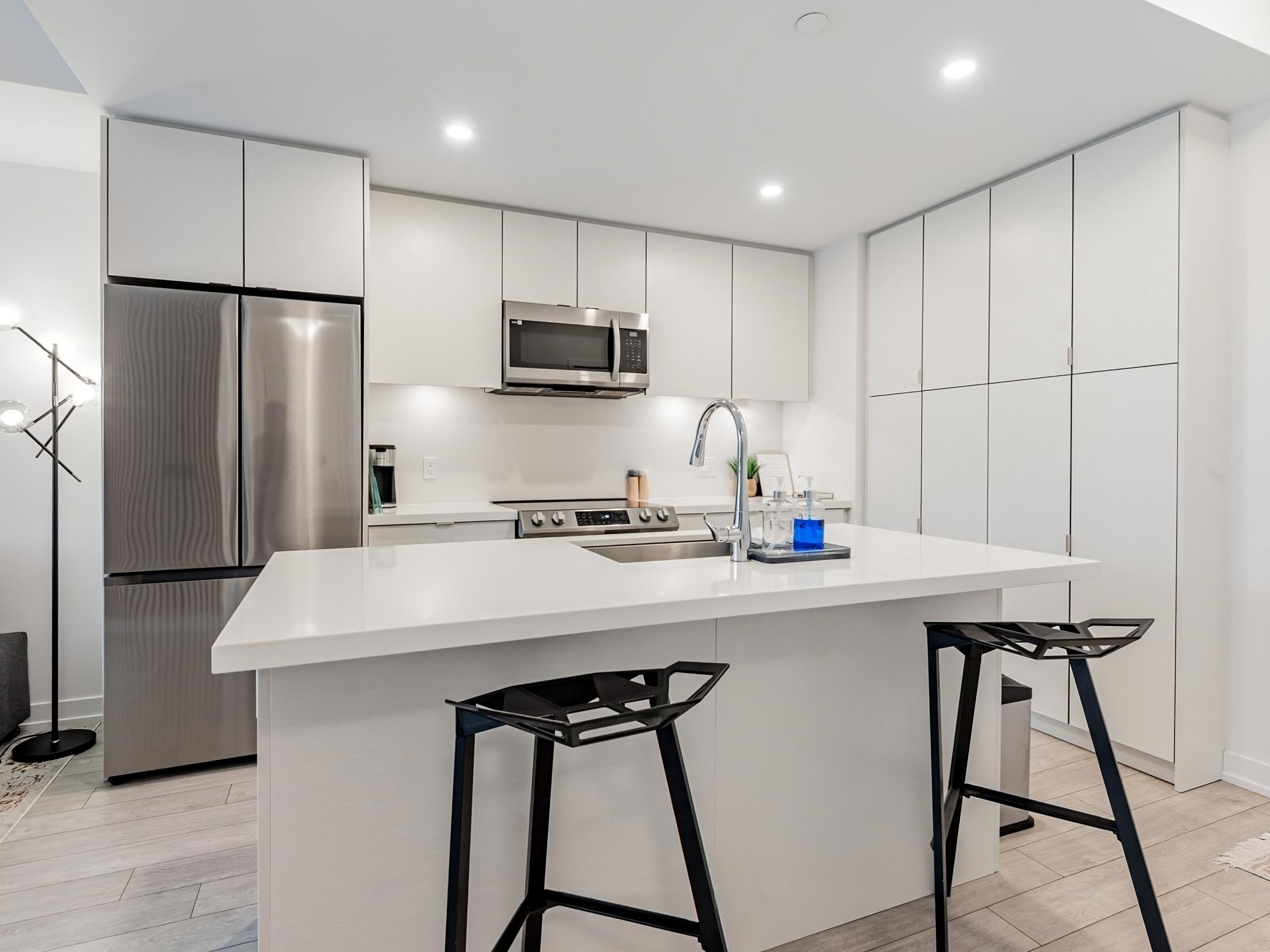 A modern kitchen with white cabinetry, stainless steel appliances, and a central island with bar stools.