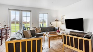 Ein geräumiges Wohnzimmer mit großem Fernseher, Ledersofas, einem Couchtisch und einem Essbereich mit Stühlen und einem Tisch.