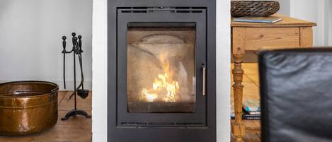 Una chimenea moderna con puerta de cristal, un mueble de madera con una cesta tejida, y un balde de metal sobre el suelo.