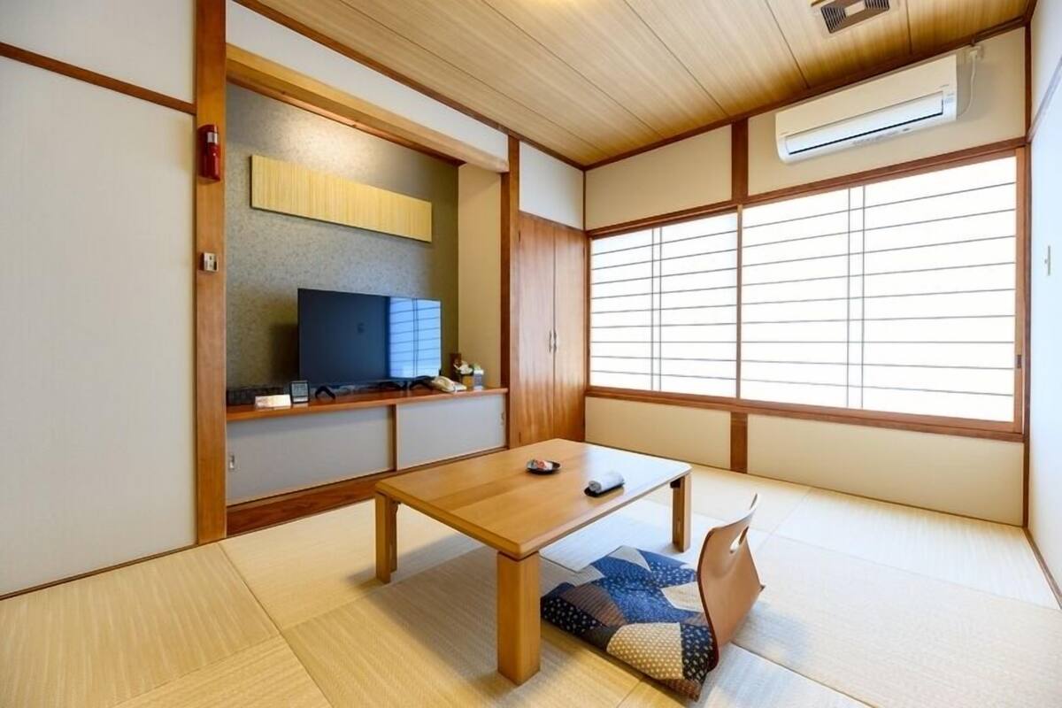 Een traditionele Japanse kamer met tatami vloerbedekking, een lage houten tafel, een televisie en schuifdeuren van shoji-papier.
