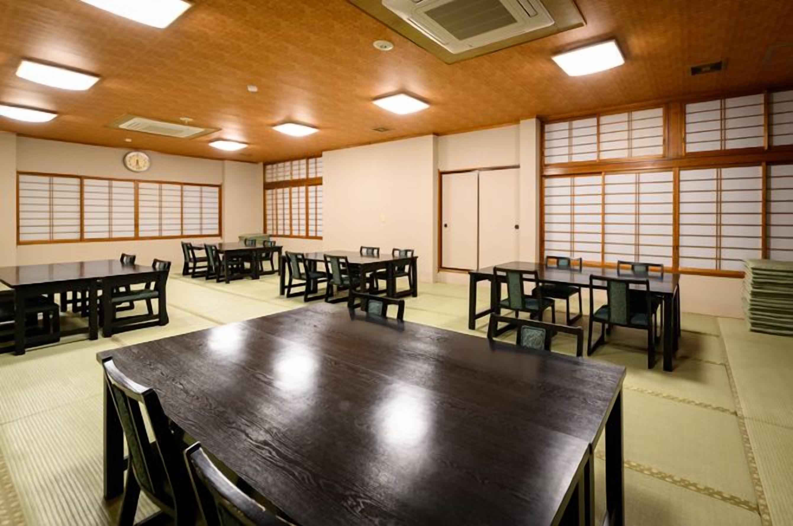 Un salón de conferencias con una gran mesa, sillas, esteras de tatami y ventanales tradicionales japoneses.