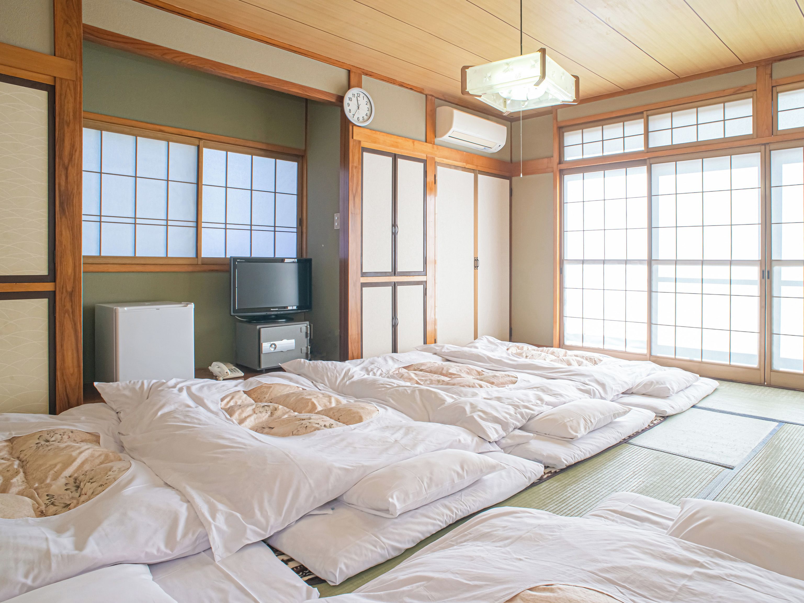 Una habitación tradicional japonesa con suelo de tatami, televisión, refrigerador y un reloj en la pared.