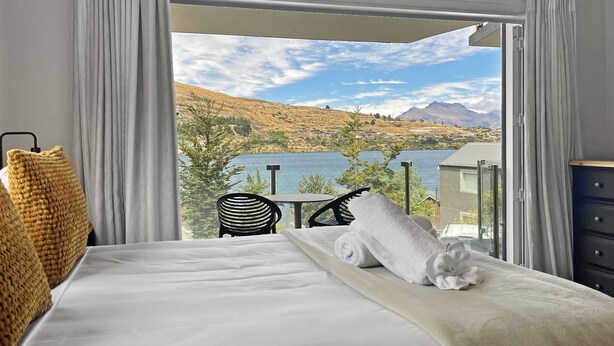 Habitación de hotel con cama, silla, mesa y vistas a un lago y montañas.