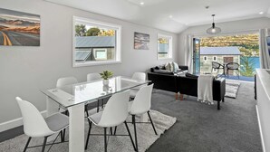 Un salón moderno con una mesa de comedor de vidrio, sillas blancas, un sofá negro y vista a un paisaje costero.