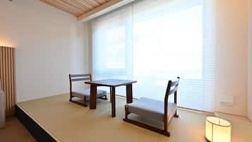 Una habitación con tatamis, una mesa baja, dos sillas, una lámpara y una ventana con persianas.