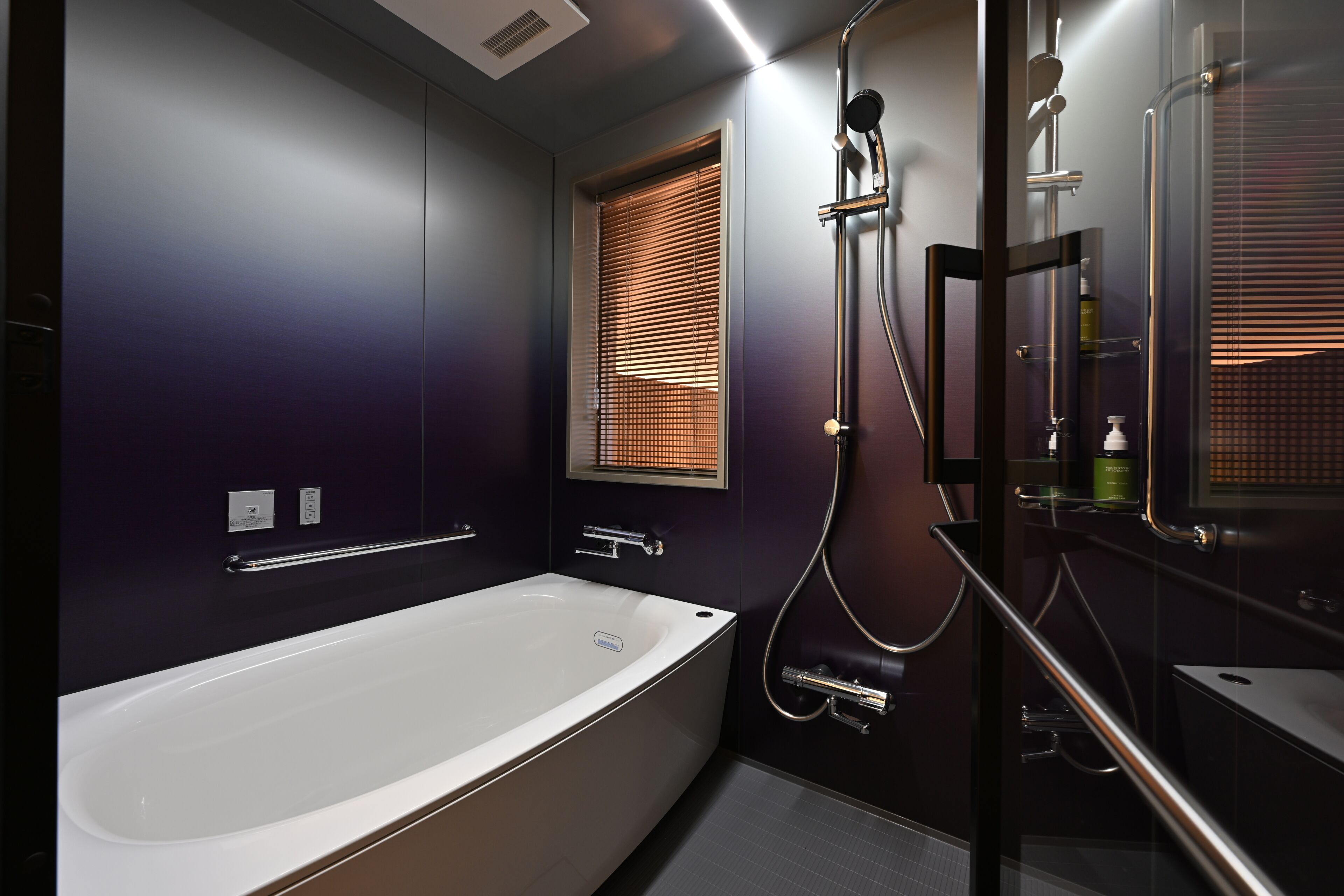 A modern bathroom with a bathtub, a glass shower enclosure, and a window with blinds.