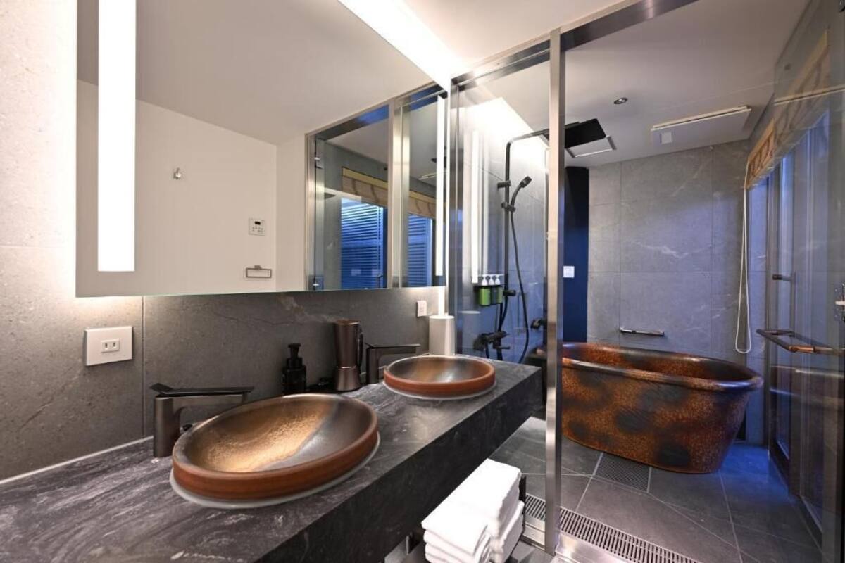 A modern bathroom with a large mirror, two round sinks, a freestanding bathtub, and a shower area.