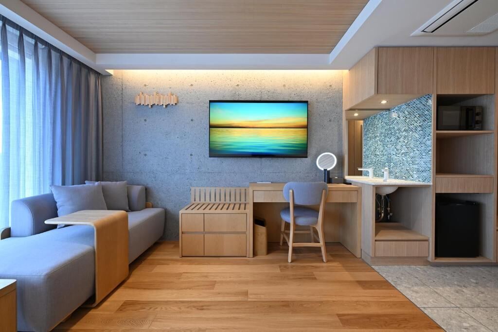 A modern room with a sofa, a desk, a chair, a TV, and a bathroom with a tiled wall.