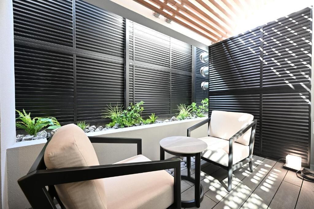 A modern outdoor seating area with a sofa and chairs, a small table, and a planter with plants.