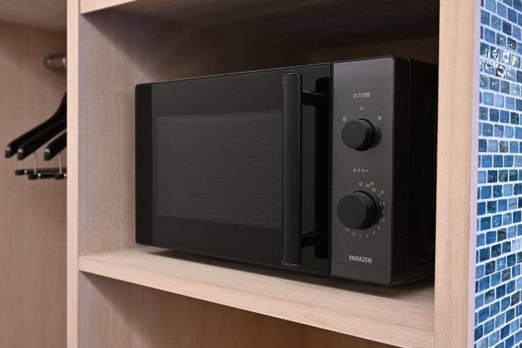 A black microwave in a wooden cabinet with a tiled backsplash.