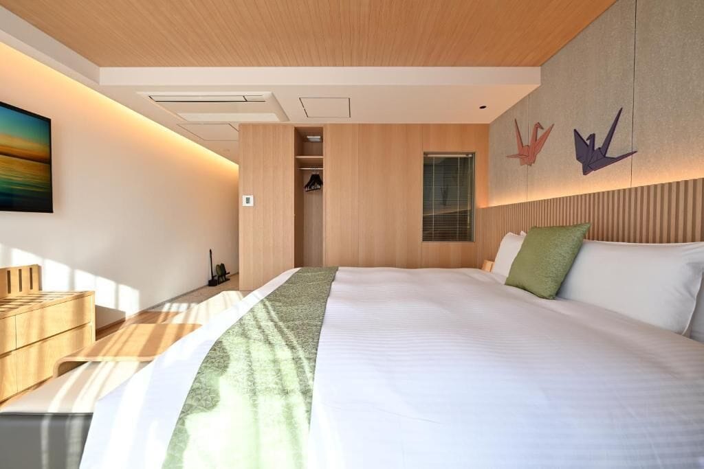 Une chambre d’hôtel moderne avec un grand lit, une tête de lit en bois, un dressing et un tableau au mur.