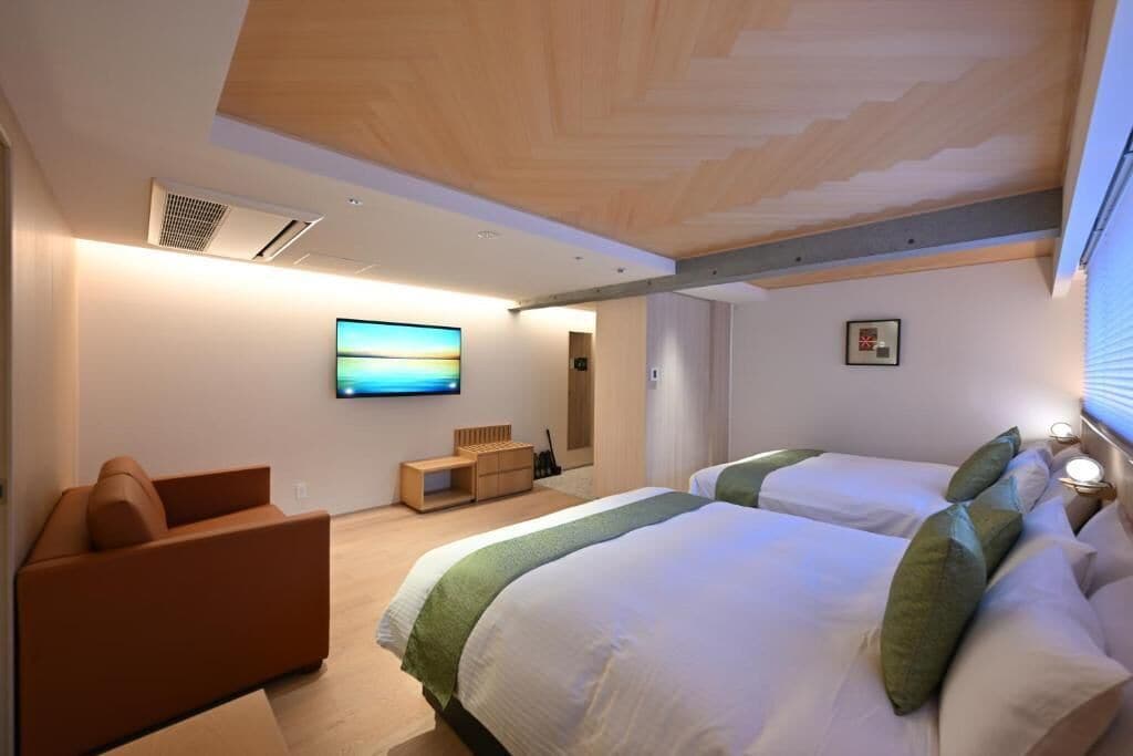 Una habitación de hotel moderna con una cama grande, un sofá, un televisor y un techo de madera.