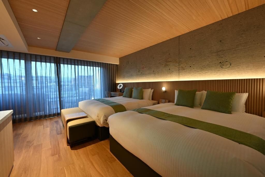Une chambre d’hôtel avec deux lits, un plafond en bois, une grande fenêtre avec des rideaux et une vue sur la ville.