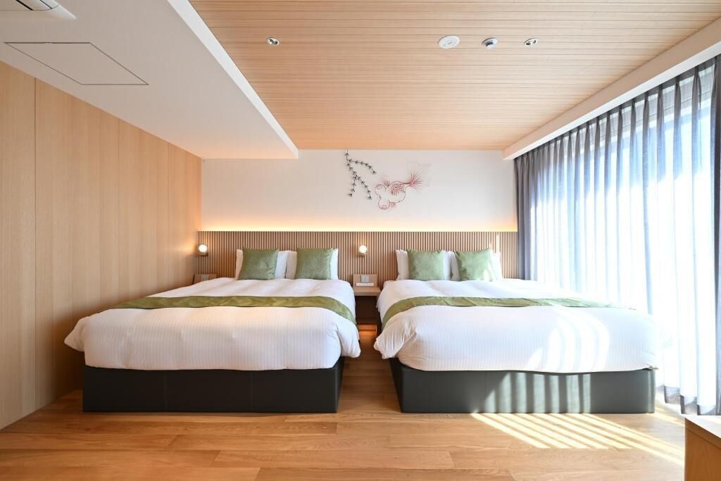 Una habitación de hotel moderna con dos camas, paneles de madera en las paredes, un techo con iluminación empotrada y un amplio ventanal con cortinas.