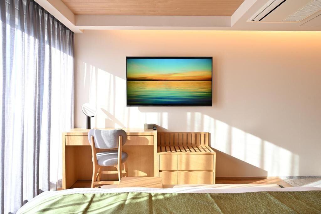 A modern bedroom with a desk, chair, and a painting of a sunset.