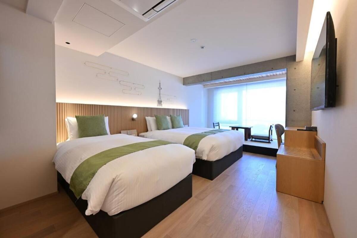 A modern hotel room with two beds, a desk, a chair, and a large window.