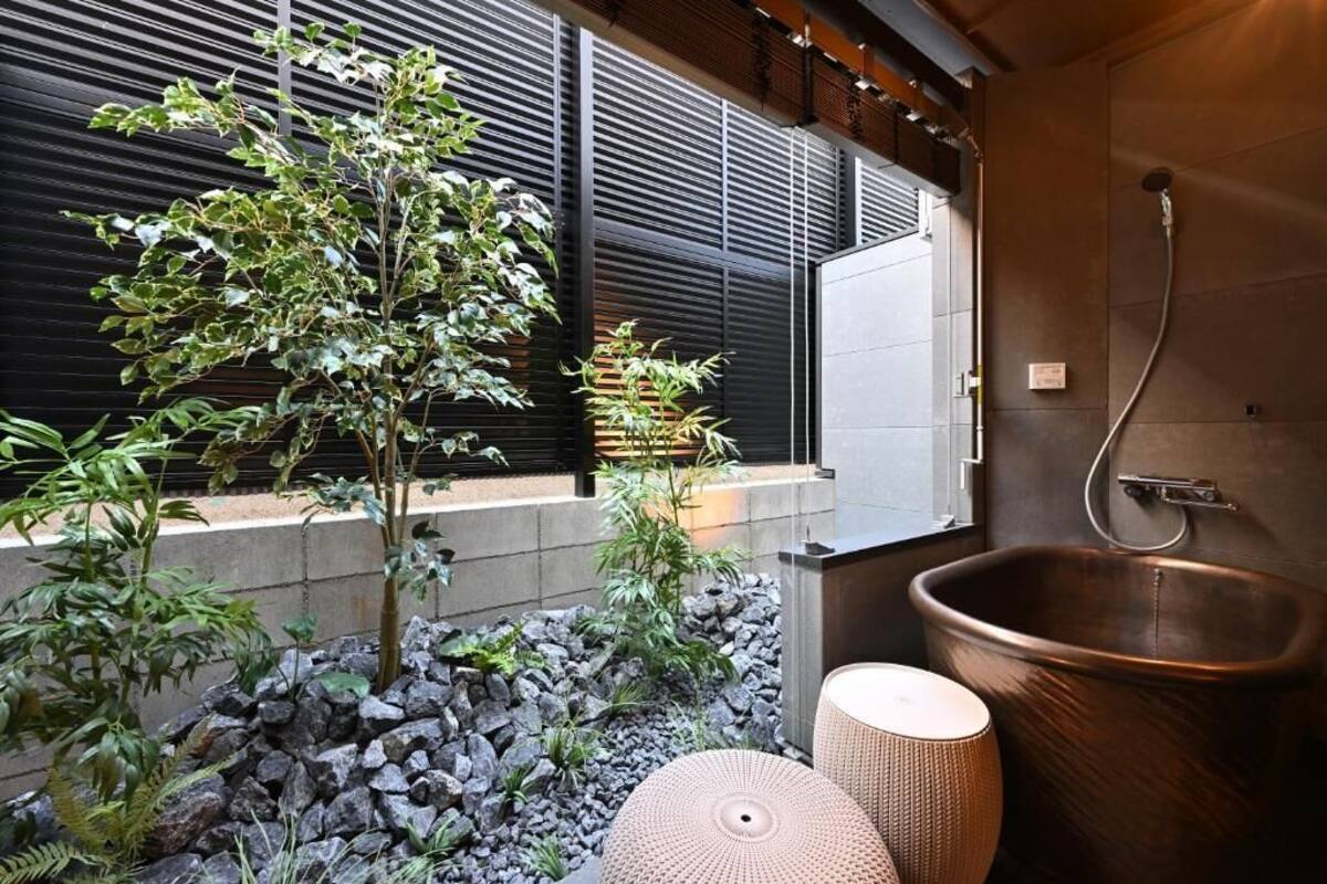 A modern bathroom with a large copper bathtub, a small round stool, and a potted plant.