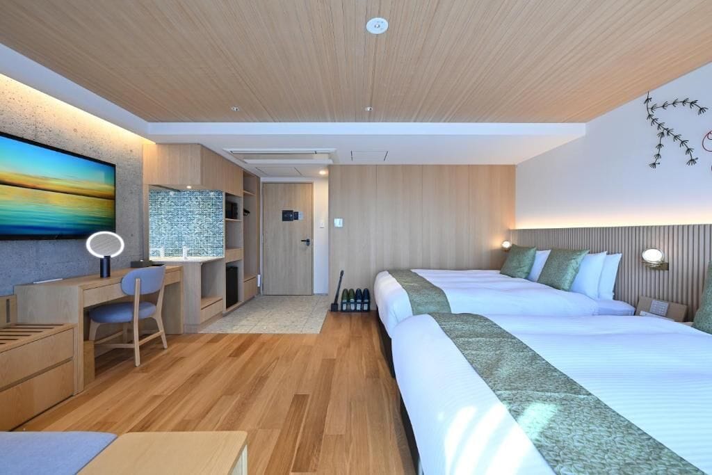 A modern hotel room with a wooden ceiling, a large bed, a desk with a chair, a TV, and a wall-mounted lamp.