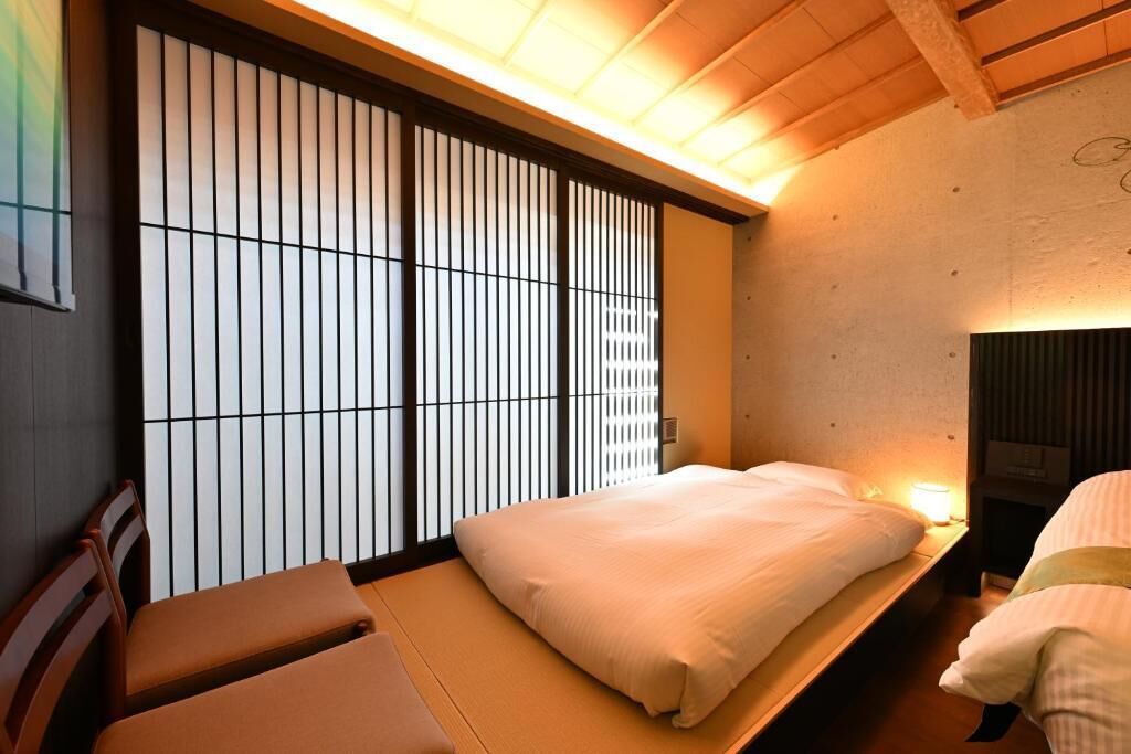 A traditional Japanese room with tatami flooring, a low bed with white bedding, and a sliding shoji screen.