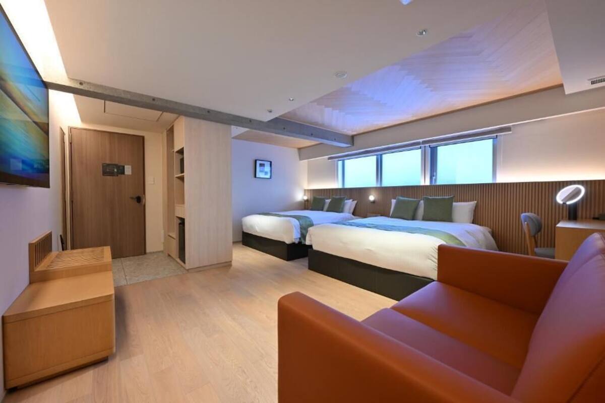A modern hotel room with a large bed, a sofa, a desk, and a view of the city.