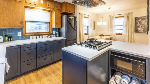 Una cocina moderna con armarios oscuros, cocina a gas, microondas integrado y refrigerador de acero inoxidable.