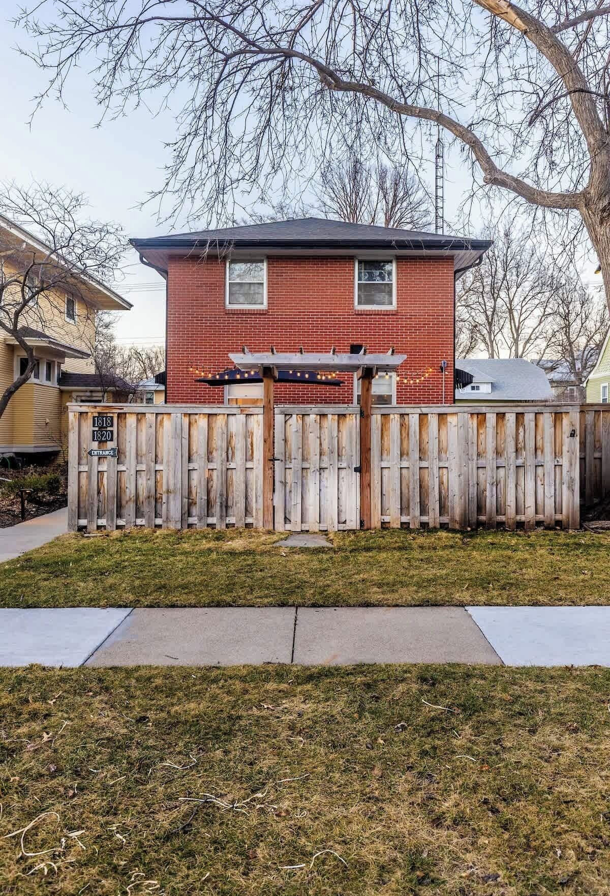 A red brick house with a wooden fence and a wooden pergola.