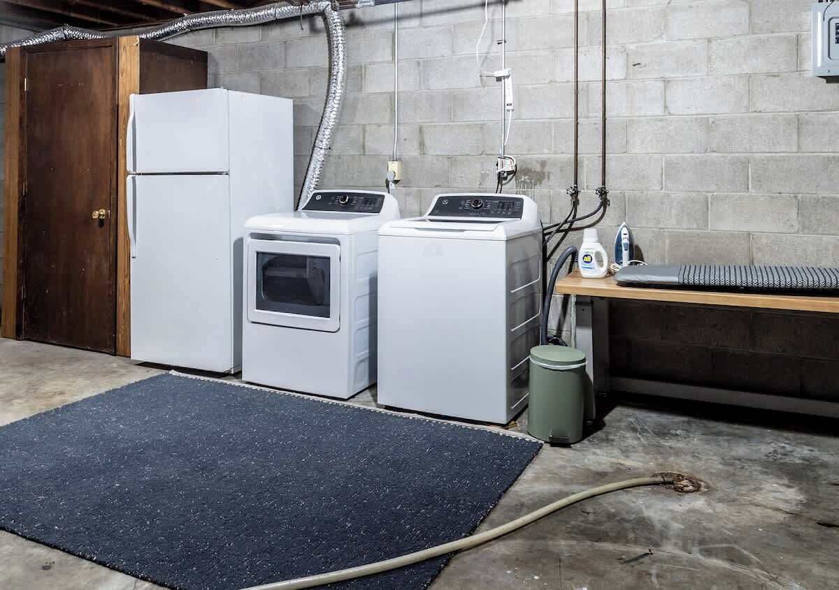 A laundry room with a refrigerator, washing machine, dryer, and a small wooden table with a keyboard.
