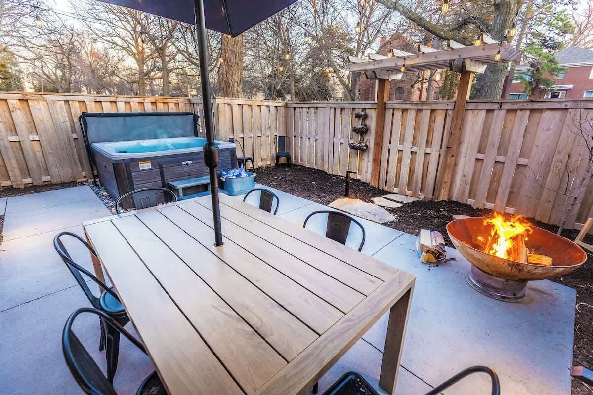 An outdoor patio with a wooden table and chairs, a hot tub, and a fire pit.