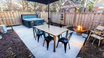 Een buitenpatio met een tafel, stoelen, een jacuzzi en een vuurkuil.