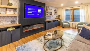 Una sala de estar moderna con una televisión de pantalla plana, estanterías empotradas, una chimenea, un sofá y una mesa de centro.