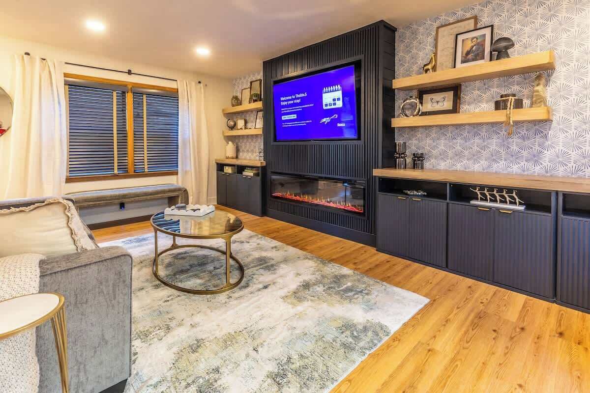 A modern living room with a flat-screen TV, a fireplace, wooden flooring, a sofa, and a coffee table.