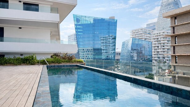 Un edificio moderno con piscina en la azotea, rodeado de estructuras de vidrio y hormigón.