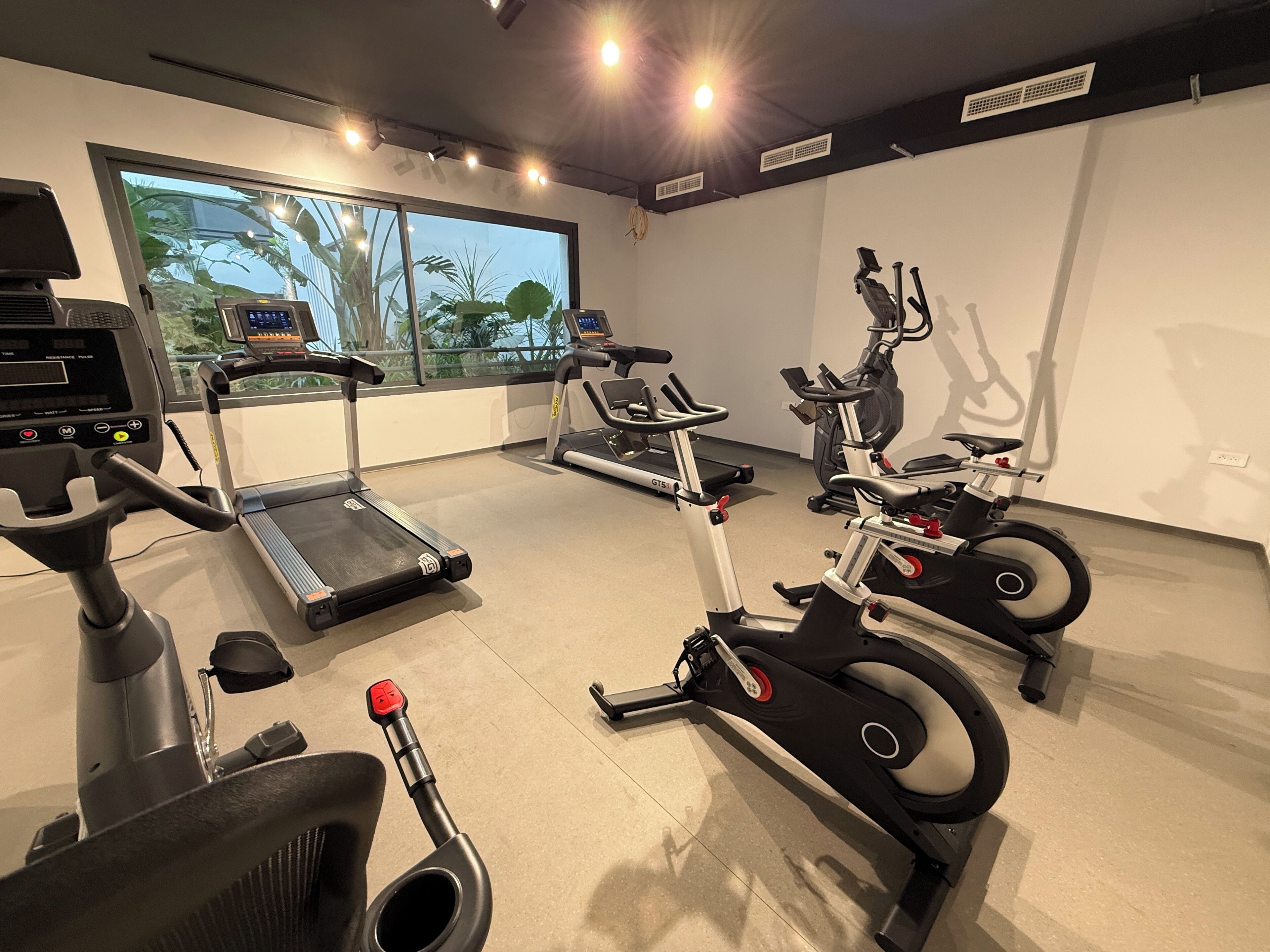Un gimnasio con cintas de correr, bicicletas estáticas y una máquina de remo.