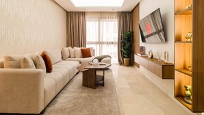 Una sala de estar moderna con un sofá modular, una mesa de centro, un televisor montado en la pared y una estantería de madera.