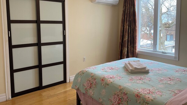 A bedroom with a bed, a window with curtains, a wall-mounted air conditioner, and a sliding door.